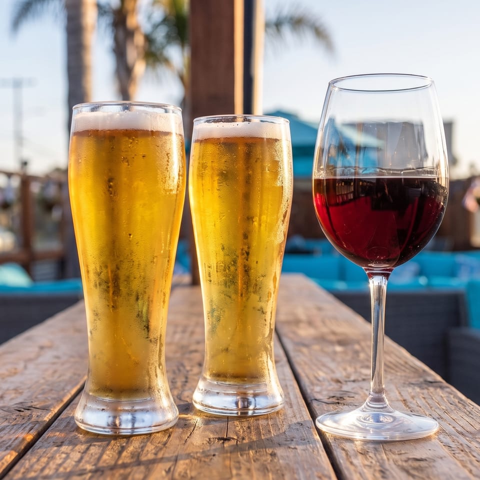 Two beers and a glass of red wine on a wooden table at an outdoor patio.