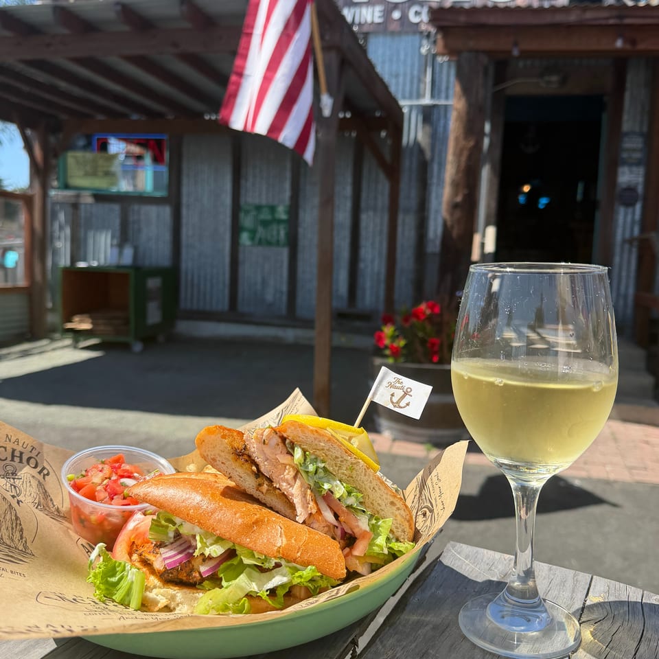 Grilled fish sandwich, pico de gallo, and white wine on an outdoor table at The Anchor restaurant.